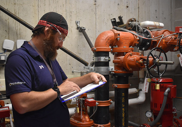 Man writing on a clip board in front of a fire protection system